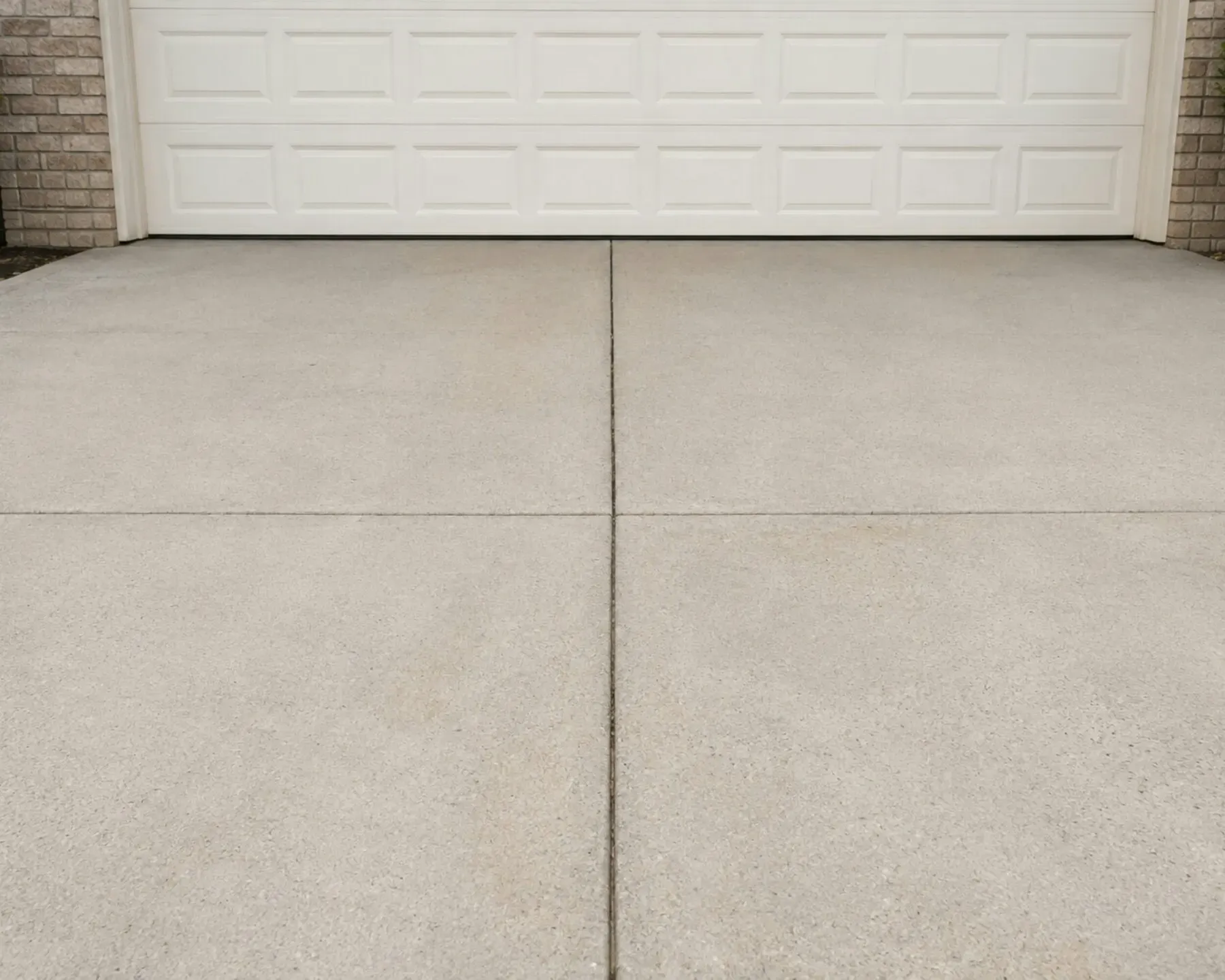 A finished plain concrete driveway leading to a garage, broom-finished with a tooled control joint